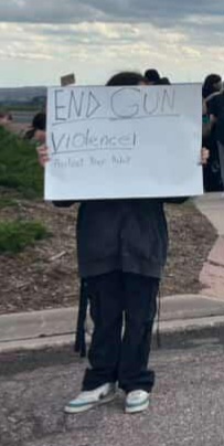 A student holding up a protest sign at King soopers.